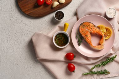 Gri arka planda domatesli, soslu ve limonlu lezzetli somon bifteği.