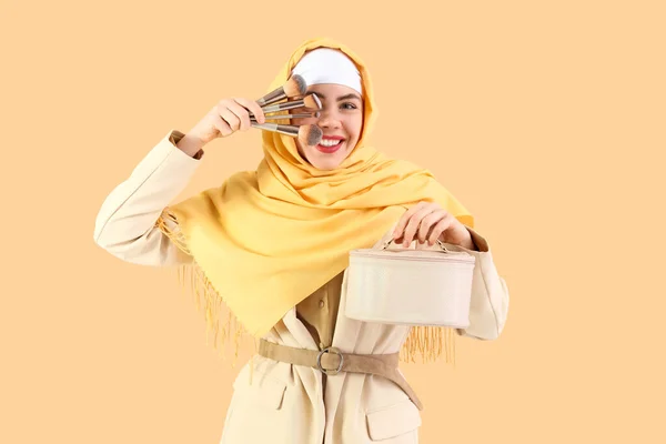 Schöne Muslimin Mit Kosmetiktasche Und Make Pinseln Auf Beigem Hintergrund — Stockfoto