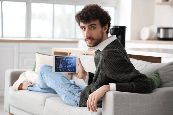 Young man with smart home security system control panel lying on sofa