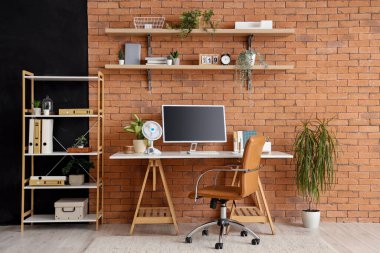 Kahverengi tuğla duvarın yanında modern bilgisayar ve elektrikli vantilatör ile rahat çalışma alanı