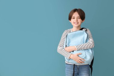 Mavi arka planda sırt çantası olan mutlu küçük çocuk.