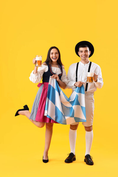 Молодая пара в традиционной немецкой одежде с пивом и баварским флагом на желтом фоне