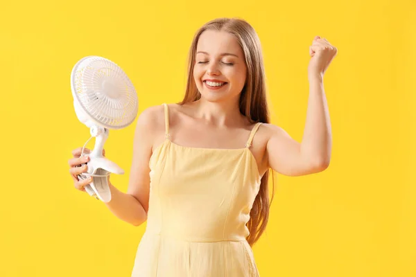 黄色の背景に電気ファンが付いている幸せな若い女性 — ストック写真
