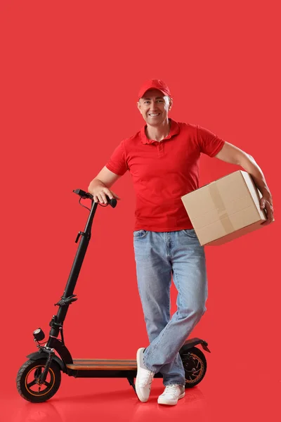 Reifer Kurier Mit Paket Und Elektrofahrrad Auf Rotem Hintergrund — Stockfoto