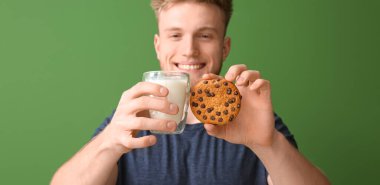 Yeşil arka planda lezzetli kurabiye ve bir bardak süt tutan genç adam.