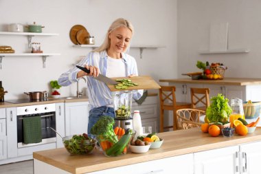 Salatalık dilimli olgun bir kadın mutfakta sağlıklı meyve suyu yapıyor.