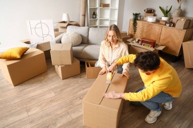Genç çift taşınma gününde odada karton kutu kaydediyor.