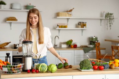Genç bir kadın mutfakta blender ile sağlıklı smoothie yapıyor.