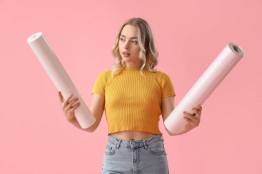 Pembe arka planda duvar kağıdı ruloları olan genç bir kadın.