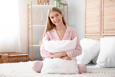 Yatak odasında oturan yumuşak yastıklı genç kadın.