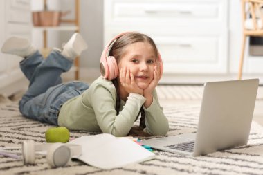 Kulaklıklı, dizüstü bilgisayarlı küçük bir kız evde bilgisayar bilimleri okuyor.