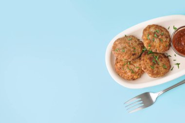 Mavi arka planda doğranmış maydanozlu pirzola, ketçap ve çatal.