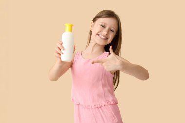 Bej arka planda güneş kremi şişesini gösteren küçük kız.