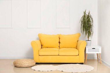 Sıcak sarı kanepe, hasır puf ve sehpa sehpanın yanındaki beyaz sehpada.