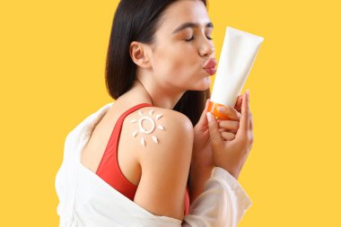 Omzunda güneş kreminden yapılmış genç bir kadın sarı arka planda öpüşüyor, yakın plan.