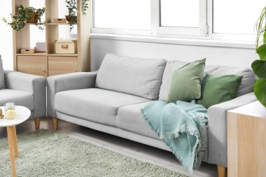 Şık gri koltukları, raf ünitesi, masa ve penceresi olan aydınlık oturma odasının içinde.