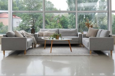 Modaya uygun gri koltukları, masası ve penceresi olan aydınlık oturma odasının içinde.