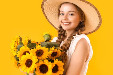 Young woman with beautiful sunflowers on yellow background