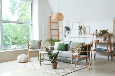 Aydınlık oturma odasının içinde bitkiler, kanepe ve koltuklar var.