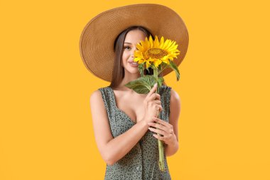 Hasır şapkalı, sarı arka planda güzel bir ayçiçeği olan genç mutlu kadın.