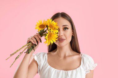 Pembe arka planda güzel ayçiçekleri olan genç bir kadın.