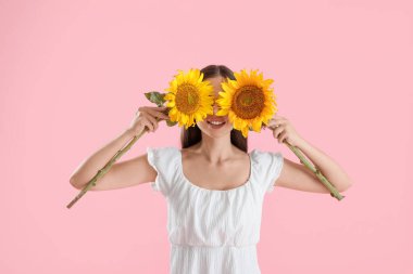 Pembe arka planda güzel kokulu ayçiçekleri olan genç ve mutlu bir kadın.
