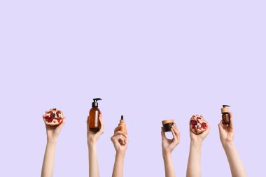 Eflatun arka planda kozmetik ürünleri ve nar tutan kadın eller