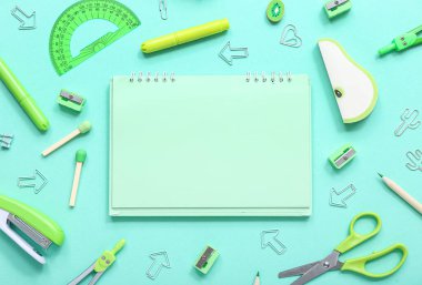 Turkuaz arka planda farklı kırtasiye malzemesi içeren defter