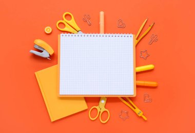 Turuncu arka planda farklı kırtasiye malzemesi içeren defterler