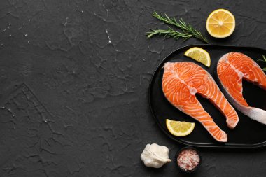 Çiğ somon biftekli tabak ve siyah arka planda farklı baharatlar.