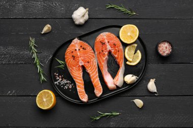 Çiğ somon biftekli tabak ve siyah ahşap arka planda farklı baharatlar.