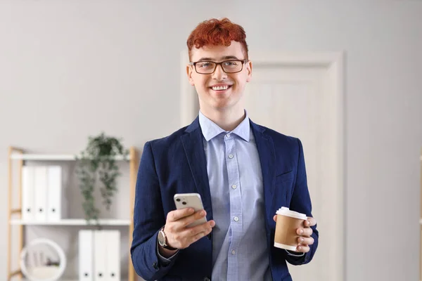 オフィスのコーヒーおよび携帯電話のコップが付いている若い赤毛のビジネスマン — ストック写真