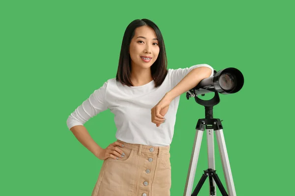 Young Asian woman with telescope on green background