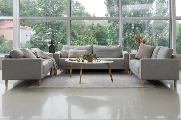 Modaya uygun gri koltukları, masası ve penceresi olan aydınlık oturma odasının içinde.