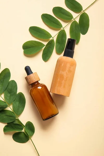 Composition with bottles of cosmetic products and acacia leaves on color background