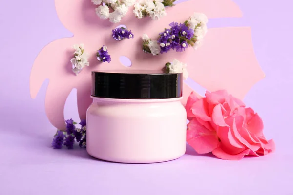 Composition with jar of cosmetic product and beautiful flowers on color background