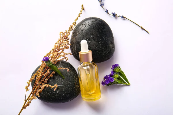 Composition with bottle of essential oil, spa stones and flowers on light background