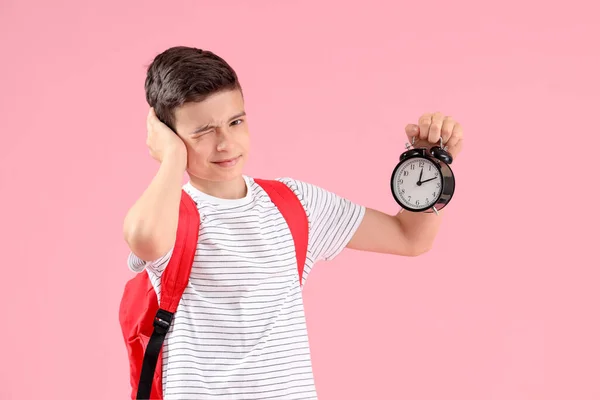 Portrait of schoolboy with backpack suffering from alarm clock sound on pink background