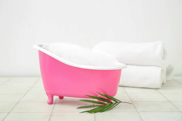 Small bathtub with foam, clean towels and palm leaf on light tile table
