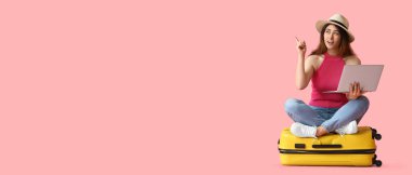 Bavulu ve dizüstü bilgisayarı olan genç bir kadın pembe arka planda mesaj için yeri olan bir şeye bakıyor.