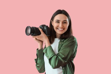 Pembe arka planda profesyonel kamerası olan kadın fotoğrafçı.