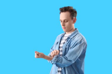 Genç adam açık mavi arka planda kolunu kıvırıyor.