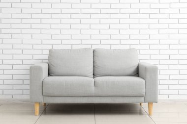 Stylish grey sofa near white brick wall