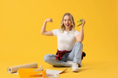 Sarı arka planda kaslarını gösteren mezuralı ve duvar kağıtlı genç bir kadın.