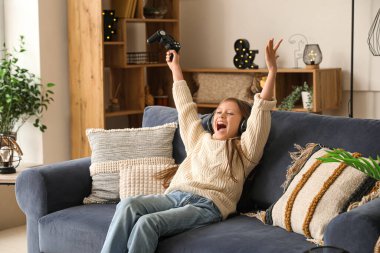 Kulaklıklı küçük kız evde video oyunu oynuyor.