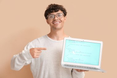 Erkek programcı bej arka planda dizüstü bilgisayarı işaret ediyor