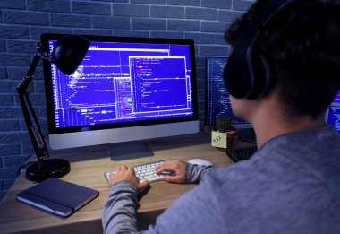 Erkek programcı geceleri ofiste kulaklık ve bilgisayarla çalışıyor.