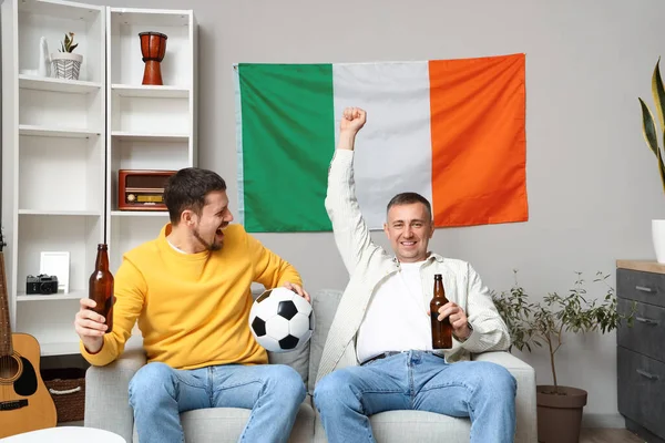 Irish men with beer and ball watching football at home
