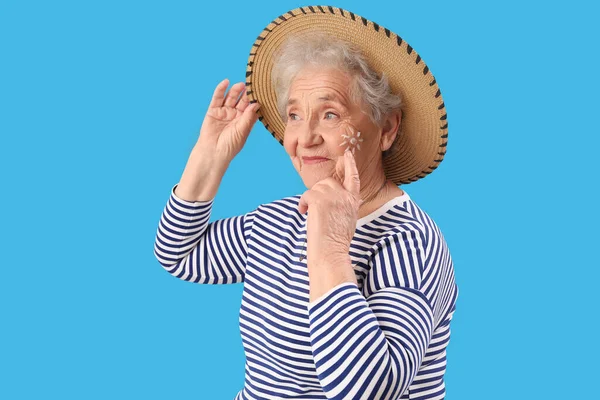 Senior woman with sun made of sunscreen cream on her face against blue background