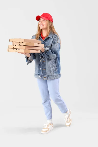 Female courier holding many pizza boxes on grey background